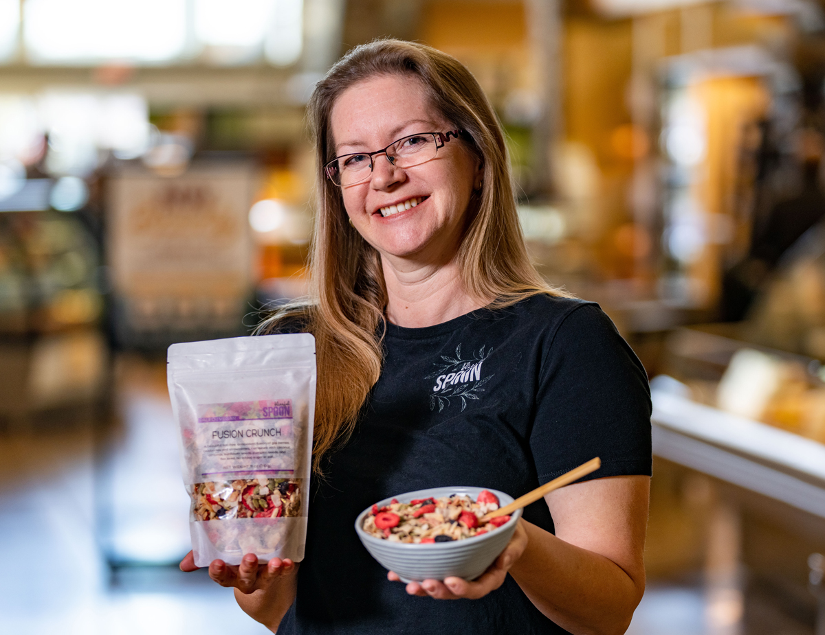 Miki Bekkari cofounder of Blissful Spoon granola holding a plastic package of Fusion Crunch granola in one hand and a bowl of granola with dried berries in the other